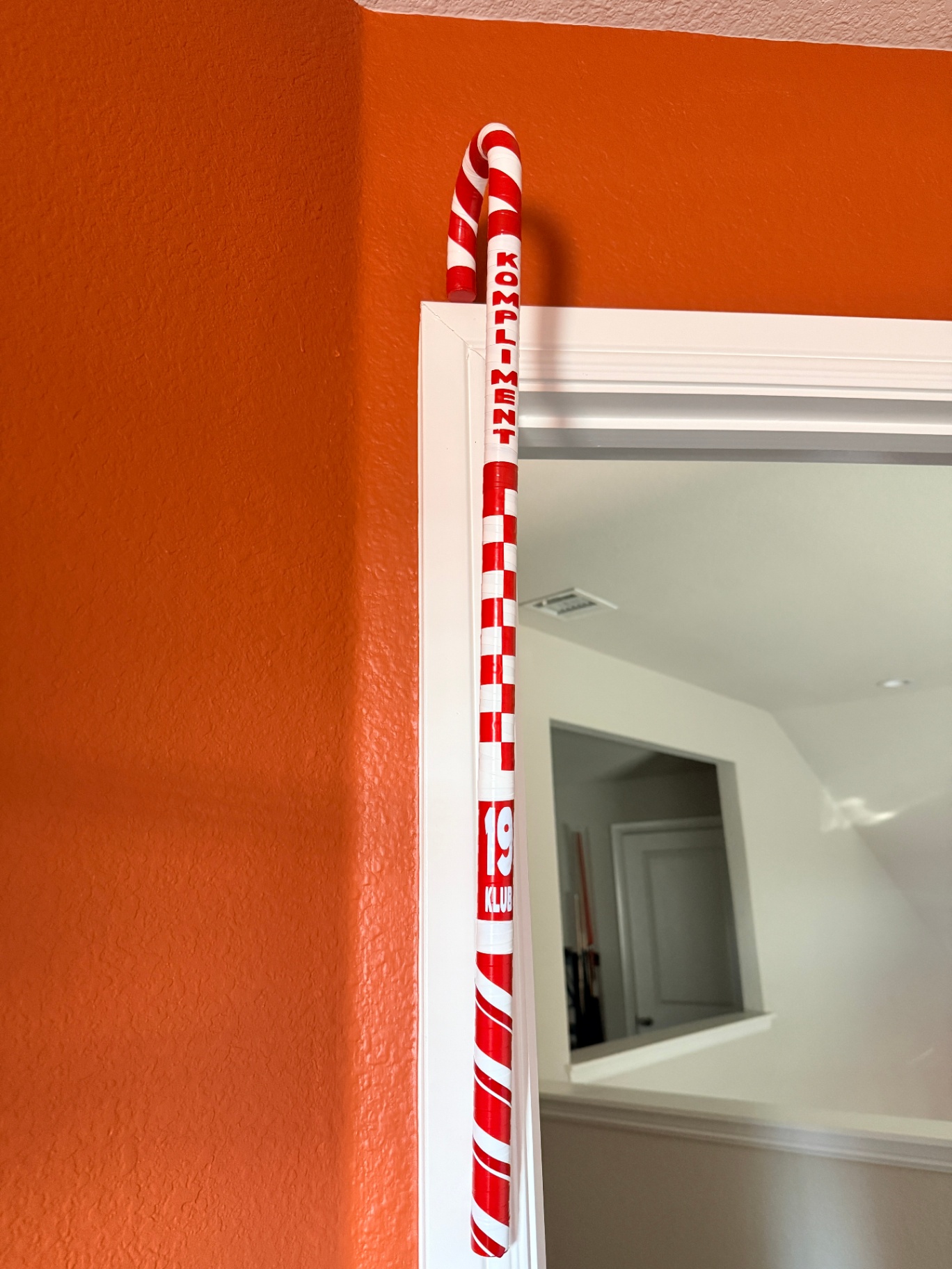 Kompliment 19 Klub cane resting on doorframe against orange wall
